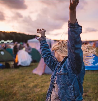 Photo d'un personne levant les bras au ciel devant des tentes