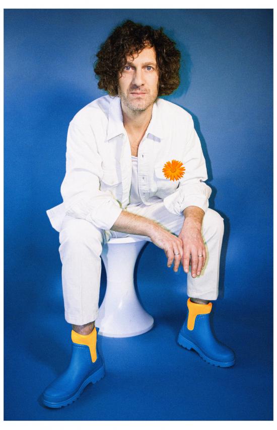 Photo de l'artiste Florent Marchet en blanc avec des bottes bleues et une fleur orange 