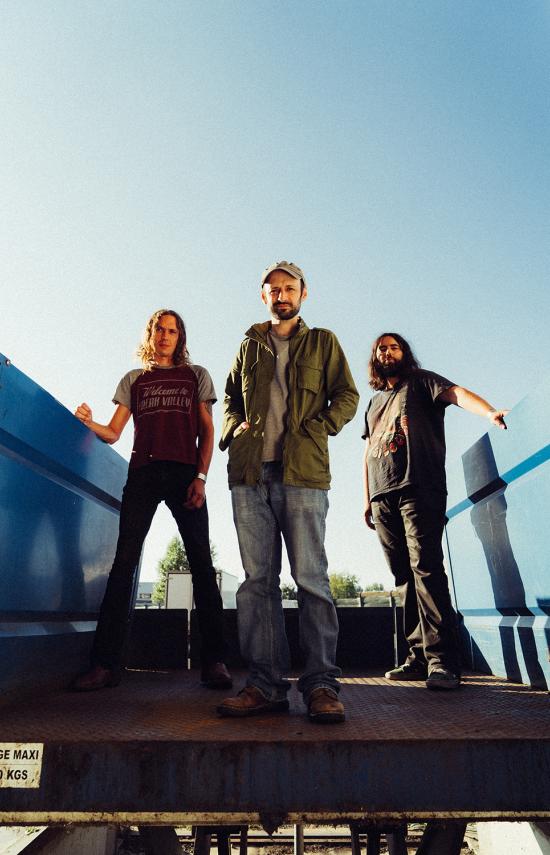 Les 3 membres du groupe Mars Red Sky sur un pont bleu avec un ciel bleu